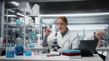 Laboratuvardaki tarih teknisyeni yapısal bozukluklar ya da safsızlıklar için ince cam kaydırağını inceliyor. Laboratuardaki kadın, mikroskop kullanarak görsel kalite kontrolü yapıyor. Kamera A.