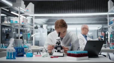 Tarih teknisyeni detaylı hücresel analiz araştırmaları için bileşik mikroskop kullanıyor. Kadın malzemeler bilim adamı modern laboratuvar tesisinde doku örneği incelemesi yapıyor. Kamera A.