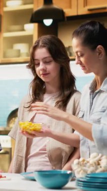 Dikey Video Ebeveynleri ve çocuklar, köy mutfağında ev yapımı pizza pişirirken, Pepperoni ve sos gibi malzemeleri hazırlarken, kahkaha ve takım çalışmasının keyfini çıkarırken eğleniyorlar. Hafta sonu aktivitesi. Kamera B.