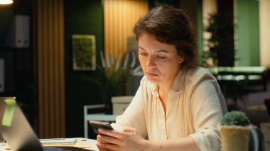 Randevu ayarlamadan önce ajandasını kontrol eden kafası karışmış bir çalışan. Mesajlara cevap vermek ve bildirileri okumak için cep telefonunu kaldırmış. Kadının dikkati dağılıyor ve kaşlarını çatıyor. Kamera B.