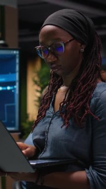 Laptop kullanan dikey video kadın teknisyeni yapay zeka sistemindeki hataları düzeltmeye çalışıyor. Teknoloji ajansının işyerindeki kadın sinir ağı hatalarını not defteriyle gideriyor