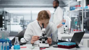 Tarih teknisyeni detaylı hücresel analiz araştırmaları için bileşik mikroskop kullanıyor. Kadın malzemeler bilim adamı modern laboratuvar tesisinde doku örneği incelemesi yapıyor, kamera B