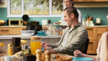 Aile kahvaltıda omlet ve hamur işlerini paylaşıyor, ebeveynler küçük oğlan ve küçük kızla omlet ve tost servisi yapıyor. Sıcaklık, rahatlama ve neşe dolu birliktelik. Kamera B.