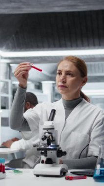 Dikey video hematoloji uzmanı. Kırmızı kan hücresi anormallikleri için kan örneklerini analiz ediyor. Sanguine sıvısı şişeleri üzerinde araştırma yapan teknisyen anemi tiplerini, kamera A 'yı teşhis ediyor.