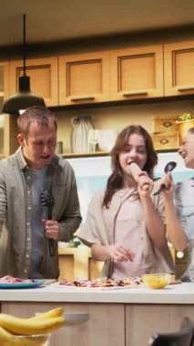 Dikey Video Ebeveynleri ve kızı yemek pişirirken karaoke yapıyor ve dans ediyor, hafta sonu etkinliği olarak ev yapımı pizza yapıyorlar. Evdeki çatal bıçaklarla şarkı söyleyen eğlenceli insanlar. Kamera A.