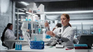 Araştırmacı saflık analizi için mavi çözeltiye tepki veriyor. Kadın sitoteknoloji uzmanı kimyasal reaksiyon özelliklerini gözlemlemek için sıvı madde ekliyor. Kamera A