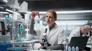 Hastalık araştırmaları klinik testleri için laboratuvar uzmanı kan örneklerini analiz ediyor. Laboratuvarda test için sanguin sıvısı şişeleri üzerinde araştırma yapan kadın bilim adamı, kamera A