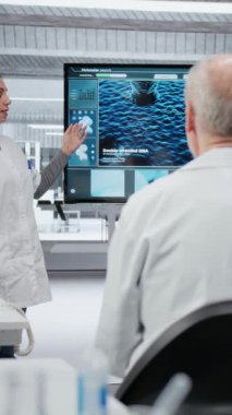 Laboratuvardaki dikey video biyoteknoloji uzmanı meslektaşlarına yenilikçi DNA dizileme projesi sunuyor. Stratejik brifing sırasında araştırmacılara 3 boyutlu biyolojik modeli gösteren laboratuar yöneticisi