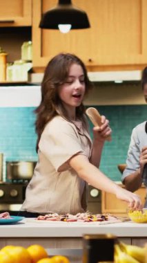 Dikey Video Ailesi mutfakta karaoke ve dans figürleriyle vakit geçiriyor, ebeveynler ve ergen kızlar ev yapımı pizzayı malzemelerle hazırlıyorlar. Kahkahalarla ve yemek hazırlıklarıyla vakit geçirmek