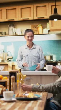 Aile kruvasan, meyve ve portakal suyuyla sofrada beklerken Dikey Video Anne kahvaltı hazırlıyor. Ebeveynler ve küçük kızları birlikte gülüyorlar, tatlım. Kamera.