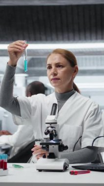 Laboratuvardaki dikey video bilimci analiz etmek için mavi sıvıyı test tüpüne koyuyor. Laboratuvar çalışanı spektroskopik analize hazırlanmak için kimyasal örnek transfer ediyor. Kamera A.