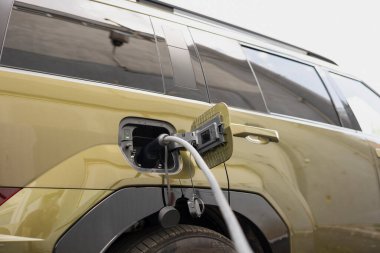 Şarj noktası istasyonunda yeşil enerji taşımacılığını gösteren elektrikli aracın yakın çekim görüntüsü. EV prizi elektrikli arabaya bağlı, sıfır emisyon teknolojisi kavramı.