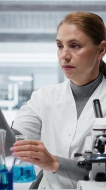 Laboratuvardaki dikey video uzmanı analiz etmek için mavi sıvıyı test tüpüne koyuyor. Moleküler biyolog, spektroskopik analize hazırlanmak için kimyasal örnek aktarıyor.