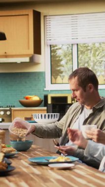 Dikey Gülümseyen Baba tablet üzerinde gülümseyen baba küçük kızıyla sohbet ediyor, ailesiyle kahvaltı yapıyor ve mutfakta güzel ev yemekleri yiyor. Beraberlik ve neşe. Kamera.