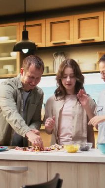 Dikey Video Neşeli Aile, ev yapımı pizza yapıyor ve kahkahalarını paylaşıyor, mozzarella ve pepperoni serpiyor. Sıcak aile aktiviteleri bağ kurmayı, takım çalışmasını ve lezzetli yiyecekleri ön plana çıkarıyor. Kamera A.