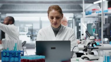 Hasta laboratuvar uzmanı baş tapınaklarını ovuyor, dizüstü bilgisayarla uğraşırken ağrıyor, genomik çalışıyor. Yorgun laboratuvar teknisyeninin yaralanması dizüstü bilgisayardaki DNA ipliği haritası, kamera B üzerinde çalışırken oldu.