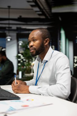 Siyahi erkek işçi bir ders kitabına büyüme stratejisi notları yazıyor. Çalışma saatleri dışında karanlık ofiste bilgi ve sezgilerle çalışıyor. Çalışan, operasyonel başarı ve verimliliği güvence altına alıyor.