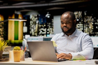 Erkek analistin veri raporlarını okuyup dizüstü bilgisayardan kontrol etmesi, proje planlaması ve mesai sonrası görevleri planlaması. Hedef başarısı için not ve el yazısı.