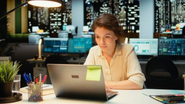 Masadaki kadın video görüşmesi sırasında kameraya gülümsüyor, dikkat ve profesyonellik. Çalışanlar sanal sohbete dalıyorlar, uzak katılımcılarla fikir alışverişinde bulunuyorlar. Kamera A.