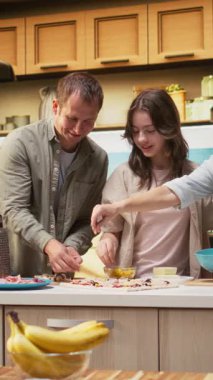 Ergen kız ve ebeveynlerin birlikte gülüp eğlendikleri ve mutfakta ev yapımı pizza hazırladıkları dikey video portresi. Neşe, aşçılık eğlencesi ve hafta sonu aktiviteleri sırasında aile bağları