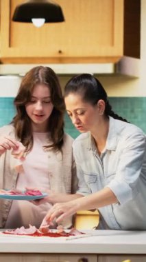 Dikey Video Şirin Ebeveynler ve çocuklar birlikte ev yapımı pizza hazırlayıp hamura salam ve jambon gibi taze malzemeler ekliyorlar. Aile bağları, mutfakta kahkahalar.