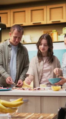 Herkes hamurun üzerine peynir ve mozzarella katarak ev yapımı pizza hazırlarken, Dikey Video Ailesi mutfakta eğleniyor. Sıcak sahne neşe ve lezzetli ev yapımı yemekleri yakalar. Kamera A.