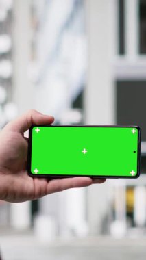 Kalabalığın hareketli sokaklarında, çok kültürlü şehir yaşamında, günlük hareketlerde ve dinamik kentsel kalabalığın aktif rutininde gezinen sıradan bir adamın dikey video krom anahtar telefonu. Başkent alanı