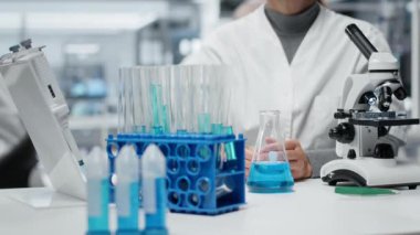 Moleküler biyolog saflık analizi için mavi çözeltiye tepki veriyor. Orta yaşlı bir kadın kimyasal reaksiyon özelliklerini gözlemlemek için test tüpüne sıvı madde ekliyor.