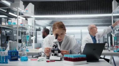 Mikroskop inceleyen dişi mikroskopist hücreleri görmek için laboratuarda cam kaydırma yapıyor. Araştırma tesisi çalışanı örnek slaytı kontrol eder, optik cihaz kullanarak görüntüleme işlemi yapar, kamera A