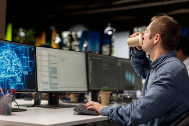 Ofiste kahve içen, yapay zeka ölçümlerini inceleyen, performans göstergelerini izleyen bir müteahhit. Teknoloji firması bilişim uzmanı kafeinli içeceklerin keyfini çıkarırken bilgisayar üzerinde program kullanarak uyanmak istiyor.