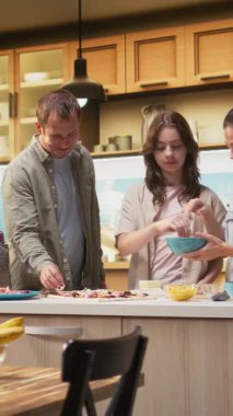 Dikey Video Ebeveynleri ve ergen mozzarella serpiştirme ve ev yapımı pizza hamurunun üzerine rendelenmiş peynir serpiştirme, mutluluk ve mutfak yaratıcılığıyla dolu bir aile anında mutfakta birlikte gülme. Kamera A.