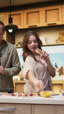 Dikey Video Ailesi mutfakta karaoke ve dans figürleriyle vakit geçiriyor, ebeveynler ve ergen kızlar ev yapımı pizzayı malzemelerle hazırlıyorlar. Kahkahalarla ve yemek hazırlıklarıyla vakit geçirmek