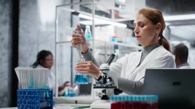 Araştırmacı saflık analizi için mavi çözeltiye tepki veriyor. Kadın sitoteknoloji uzmanı kimyasal reaksiyon özelliklerini gözlemlemek için sıvı madde ekliyor. Kamera B