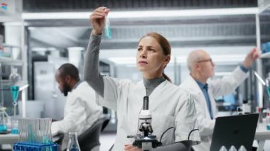 Tıbbi laboratuvar teknisyeni test tüpündeki mavi sıvı kimyasal özellikleri inceliyor. Araştırma tesisi çalışanı yeni bileşik içeren şişeyi tutuyor, tıbbi araştırma ve geliştirme, kamera B