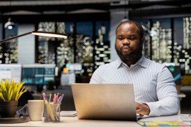 Siyahi adam mali numaraları kontrol ediyor, strateji odasında arşivlenmiş dosyaları inceliyor. Raporların değerlendirilmesi, araştırma ve düzenleme gündemi.