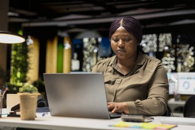 Odaklanmış Afrikalı Amerikalı kız veri raporlarını araştırıyor ve iş amaçlarına ulaşmak için hedefler tasarlıyor, tashih için hesap tablolarını kullanıyor. Kadın mesai saatleri dışında şirket için çalışıyor..