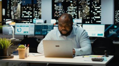 Afrika kökenli Amerikalı iş adamı ofiste duruyor ve çözümler arıyor, düşünceli olarak ve şirket büyümesi için yeni fikirler buluyor. Gece geç saatlerde görevleri öngören danışman.