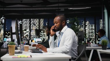 Afrika kökenli Amerikalı iş analisti gece geç saatlerde bir telefon görüşmesi yapıyor. Programın geleceğinden emin olmak için. Ortağıyla telefonda konuşuyor. Profesyonellik gösteren meşgul bir yönetici.
