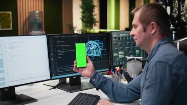 Yüksek katlı ofiste yapay zeka algoritmaları geliştirmek için bilişim uzmanı tarafından kullanılan yeşil ekran model akıllı telefon. Renkli anahtar cep telefonu kullanmak için sinirsel ağ modellerini hata ayıklamaya ara veren yönetici, kamera A