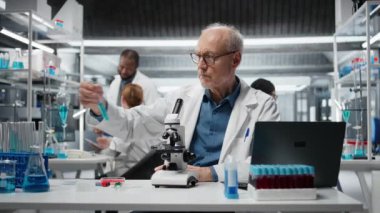 Test tüpündeki mavi sıvı polimer özelliklerini araştıran neşeli yaşlı laboratuvar çalışanı. Neşeli kıdemli laboratuvar biyoloğu yeni sentetik madde dayanıklılığını ve viskozitesini test ediyor. Kamera A