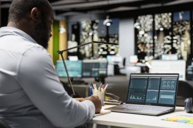 Afro-amerikan iş analisti şirket hedeflerine ulaşmak için pazar verilerini belgeliyor, bilgisayardaki bilgi grafiklerini kullanarak kontrol ediyor. Saatler sonra çok uluslu bir şirkette çalışıyorum..