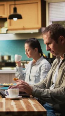 Dikey Videolu Baba kahvaltı masasında kızını görmezden geliyor ve işine odaklanıyor, laptopta bilgi yazıyor ve endişeli görünüyor. Mesafeli çalışan bir baba ve genç bir kız çocuğu.