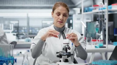 Moleküler biyolog laboratuardaki detaylı hücresel analiz araştırmaları için bileşik mikroskop kullanıyor. Modern laboratuvar tesisinde doku örneği incelemesi yapan kadın kalite kontrol analisti, kamera B