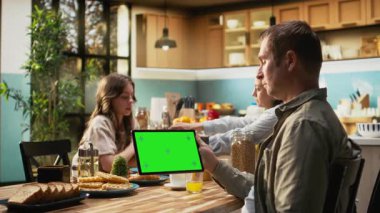 Babamla tabletteki maket ekranı ailesiyle birlikte mutfakta kahvaltı için toplandı. Anne ve babalar kahve ve portakal suyu içerken, genç kız pasta ve ev yapımı yemeğin tadını çıkarıyor. Kamera A.