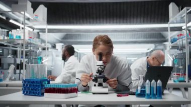 Tıbbi laboratuvardaki moleküler biyolog hücresel analiz için bilimsel mikroskop kullanıyor. Laboratuvarda optik cihaz teçhizatı ve kamera A ile örnek inceleme yapan kadın araştırmacı.