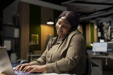 İş kadını, uzaktan görüşme için telefon görüşmesine cevap veriyor. Telefon hattındaki ortak bir sohbete katılırken gülümsüyor. Profesyonel bağlantı için uyum ve özen.