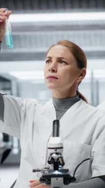 Dikey video laboratuvar teknisyeni test tüpündeki mavi sıvı kimyasal örnekleri inceliyor. Araştırma tesisi çalışanı yeni bileşik içeren şişeyi tutuyor, tıbbi araştırma ve geliştirme, kamera B