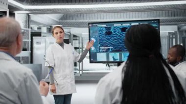 Laboratuvarda biyoteknoloji uzmanı meslektaşlarına yenilikçi DNA dizileme projesi sunuyor. Stratejik brifing sırasında araştırmacılara 3 boyutlu biyolojik modeli gösteren laboratuar yöneticisi, kamera A