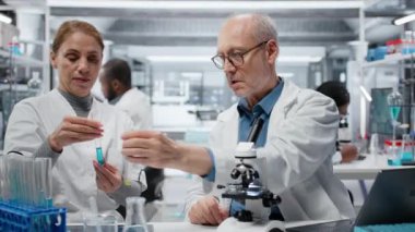 Laboratuar şefi stajyere test tüpünde sıvı polimer özelliklerini analiz etmeyi öğretiyor. Kıdemli bilim adamı, laboratuvarda yeni sentetik materyal viskozitesini test etmek için stajyer eğitmenlik yapıyor. Kamera B