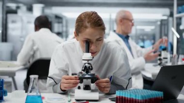 Hücresel analiz için bilimsel mikroskop kullandıktan sonra yorgun biyologlar tıp laboratuarında geriliyor. Yorgun bilim adamı çalışma masasında dinleniyor, optik cihaz teçhizatı ve kamera B ile numuneleri inceliyor.